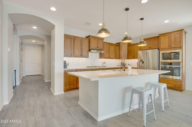 kitchen with tasteful backsplash, brown cabinets, a sink, stainless steel appliances, and under cabinet range hood