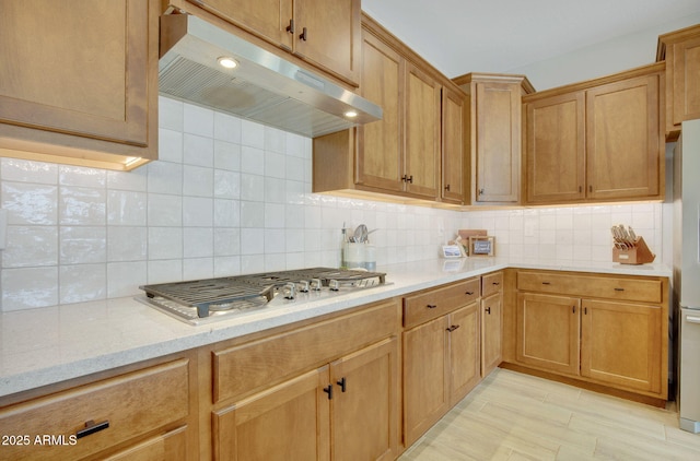 kitchen with light stone countertops, appliances with stainless steel finishes, backsplash, and under cabinet range hood