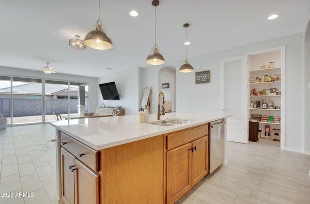 kitchen with stainless steel dishwasher, light stone counters, a sink, open floor plan, and a center island with sink