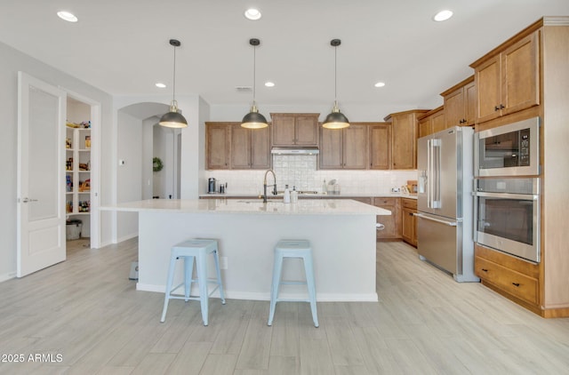 kitchen with decorative backsplash, a breakfast bar, under cabinet range hood, appliances with stainless steel finishes, and brown cabinets