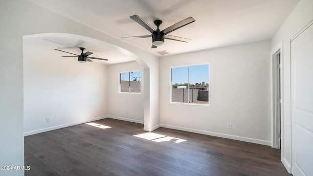 unfurnished room with visible vents, baseboards, dark wood finished floors, arched walkways, and ceiling fan