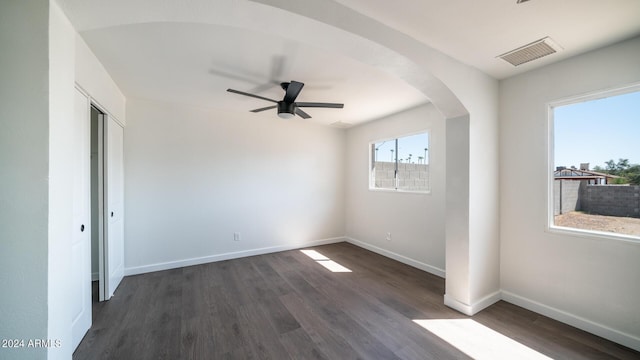 empty room featuring dark wood-style floors, visible vents, baseboards, and a ceiling fan