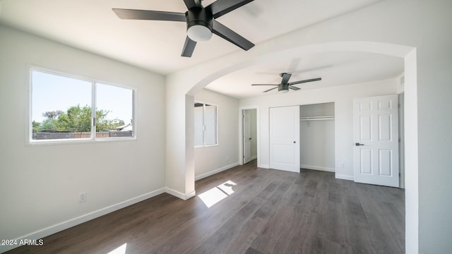 unfurnished bedroom with arched walkways, a closet, baseboards, and wood finished floors