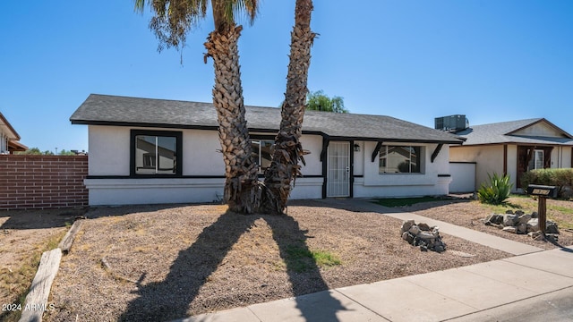 view of front of property featuring roof with shingles, fence, central AC unit, and stucco siding