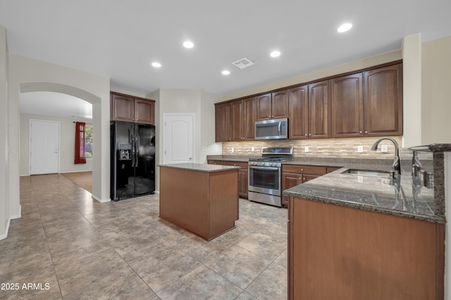 17429 W Red Bird Rd, Surprise, AZ 85387 - kitchen featuring a center island, dark stone counters, arched walkways, a sink, and appliances with stainless steel finishes