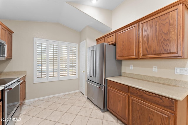 kitchen with brown cabinetry, appliances with stainless steel finishes, vaulted ceiling, light countertops, and light tile patterned flooring
