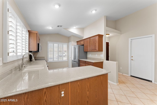 kitchen with lofted ceiling, a sink, visible vents, freestanding refrigerator, and brown cabinetry