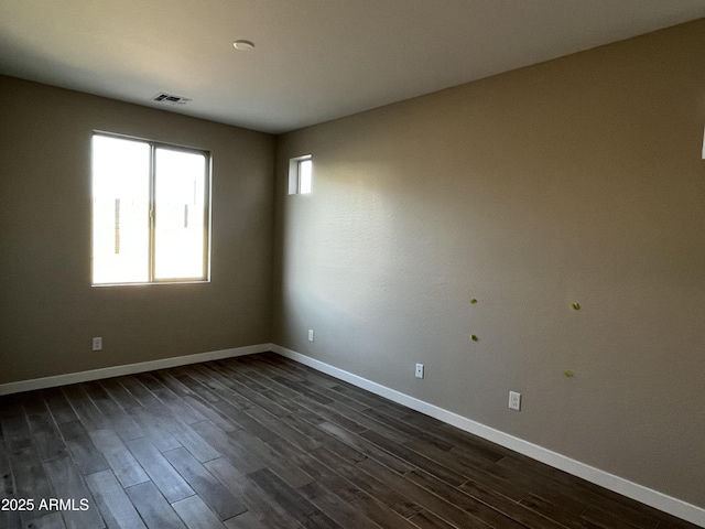 empty room featuring dark wood-style floors, visible vents, a healthy amount of sunlight, and baseboards