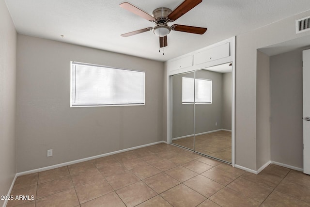 unfurnished bedroom with a closet, light tile patterned floors, a ceiling fan, and baseboards