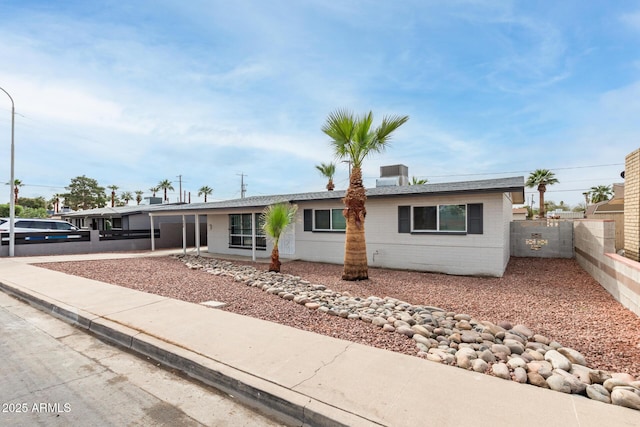 ranch-style home featuring central AC unit, concrete driveway, concrete block siding, and fence