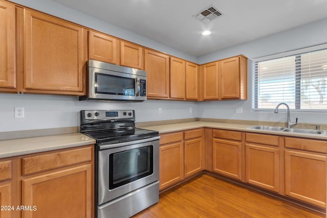 kitchen with appliances with stainless steel finishes, sink, and light wood-type flooring