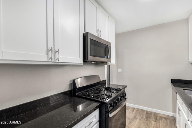 kitchen with light wood-type flooring, dark stone counters, white cabinets, and black gas stove