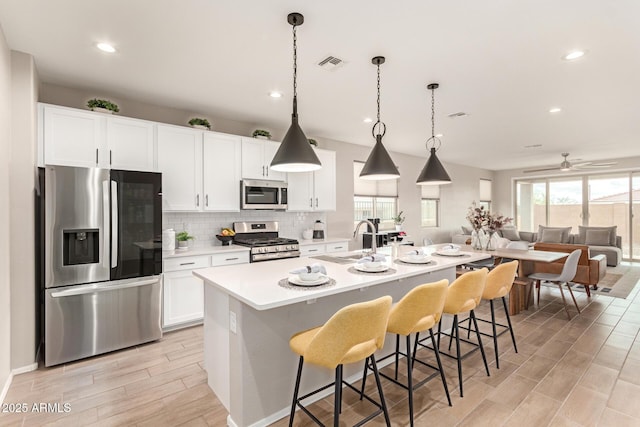 kitchen with tasteful backsplash, visible vents, stainless steel appliances, white cabinetry, and a sink