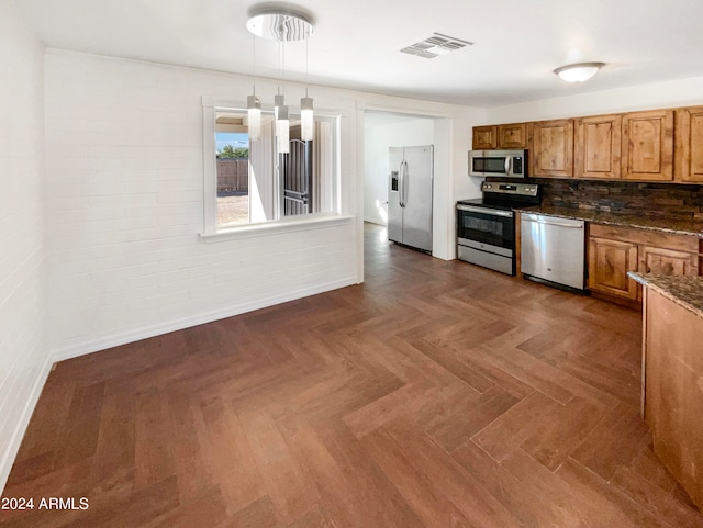 kitchen with pendant lighting, dark stone counters, stainless steel appliances, backsplash, and dark parquet flooring