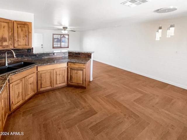 kitchen with dark stone counters, sink, kitchen peninsula, hanging light fixtures, and dark parquet floors