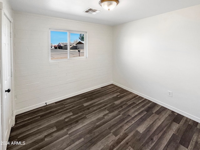 spare room with brick wall and dark wood-type flooring