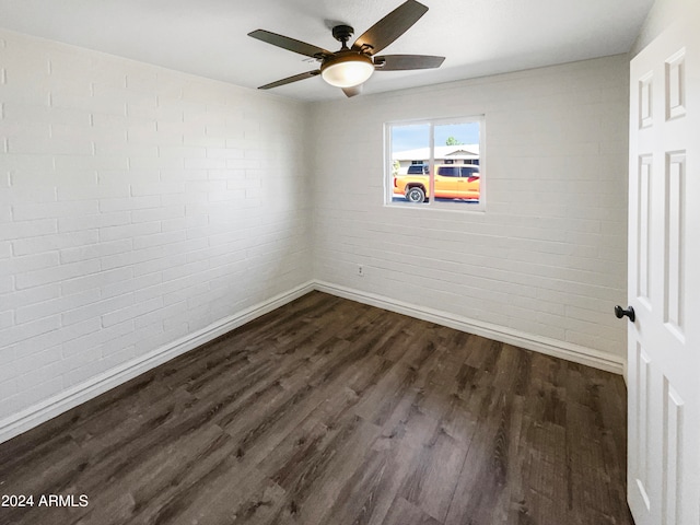 empty room with brick wall, dark wood-type flooring, and ceiling fan