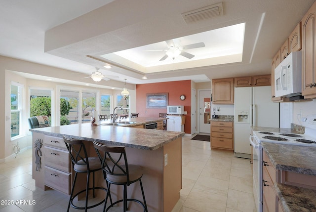 kitchen featuring a kitchen bar, a raised ceiling, white appliances, a large island with sink, and sink