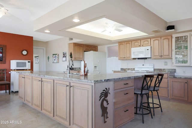 kitchen featuring a center island with sink, ceiling fan, white appliances, light stone counters, and a breakfast bar