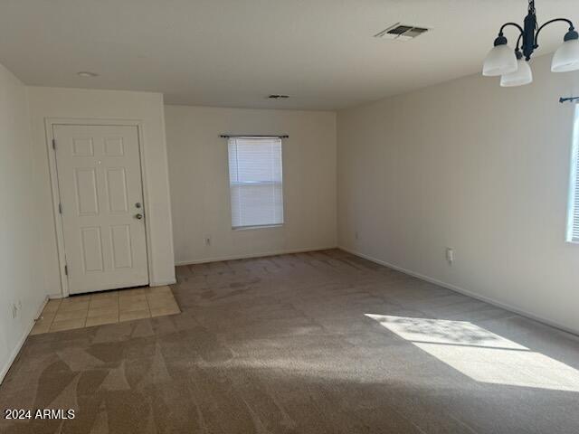 spare room featuring a chandelier, a healthy amount of sunlight, and light carpet