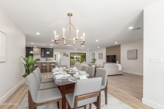 dining room with a chandelier, light wood-type flooring, visible vents, and baseboards