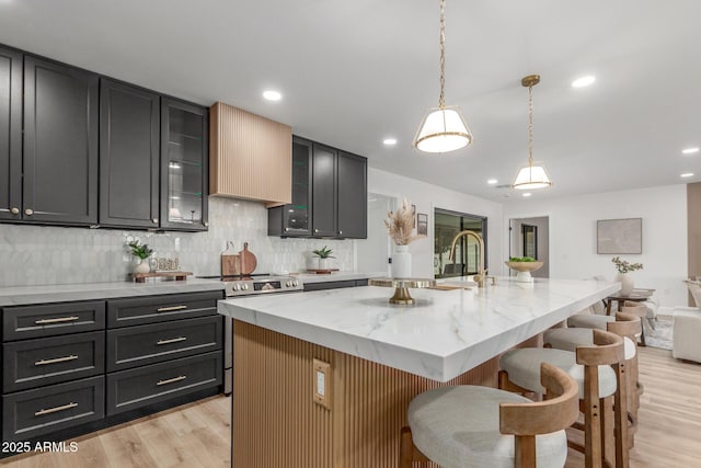 kitchen featuring a kitchen breakfast bar, decorative backsplash, stainless steel electric range, light wood-type flooring, and light stone countertops