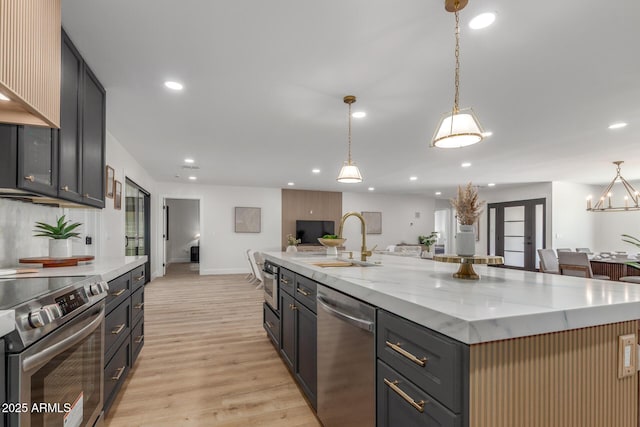 kitchen featuring a sink, light wood-style floors, a large island, appliances with stainless steel finishes, and light stone countertops