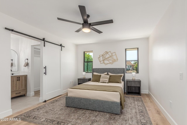 bedroom featuring a barn door, connected bathroom, ceiling fan, light wood finished floors, and baseboards