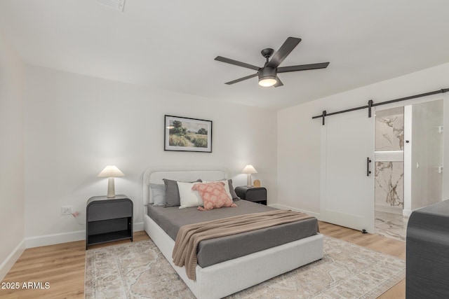 bedroom with a barn door, light wood finished floors, baseboards, and ceiling fan