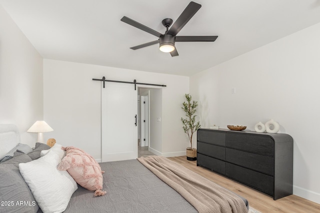 bedroom with a barn door, baseboards, a ceiling fan, and light wood finished floors