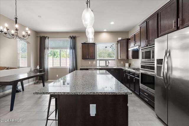 kitchen with pendant lighting, light stone countertops, appliances with stainless steel finishes, and a kitchen island