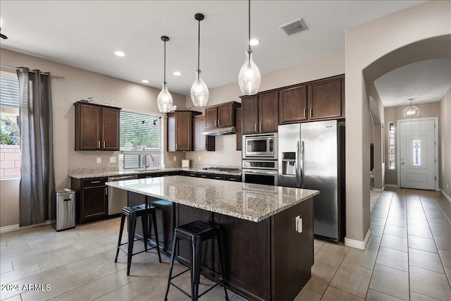 kitchen featuring a kitchen island, decorative light fixtures, sink, light stone countertops, and appliances with stainless steel finishes