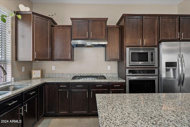 kitchen featuring stainless steel appliances, dark brown cabinetry, light stone counters, and sink