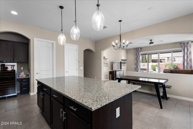 kitchen featuring light stone counters, a center island, beverage cooler, ceiling fan with notable chandelier, and decorative light fixtures