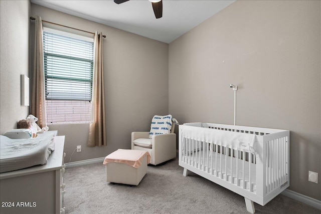 carpeted bedroom featuring a nursery area and ceiling fan