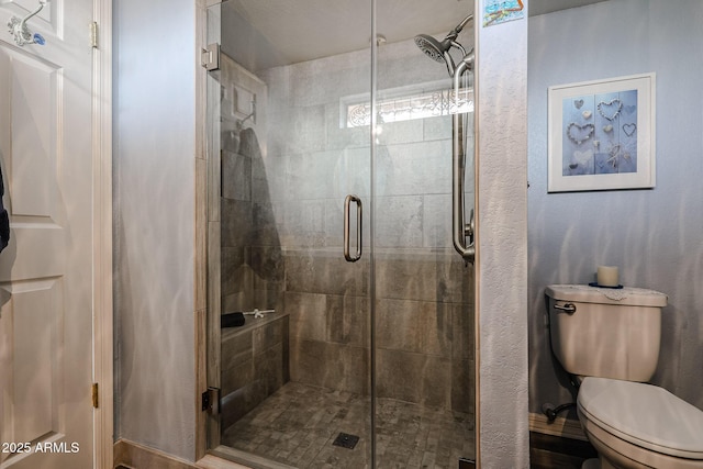 bathroom featuring a shower with door and toilet