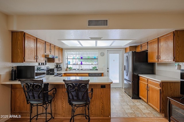 kitchen with appliances with stainless steel finishes, a kitchen breakfast bar, kitchen peninsula, and a wealth of natural light