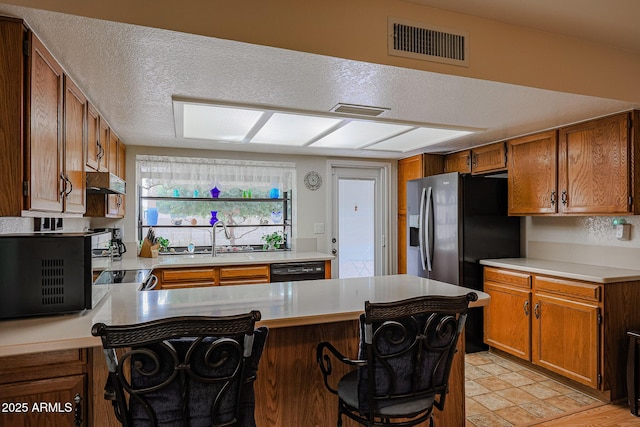 kitchen with sink, a breakfast bar, black appliances, a textured ceiling, and kitchen peninsula