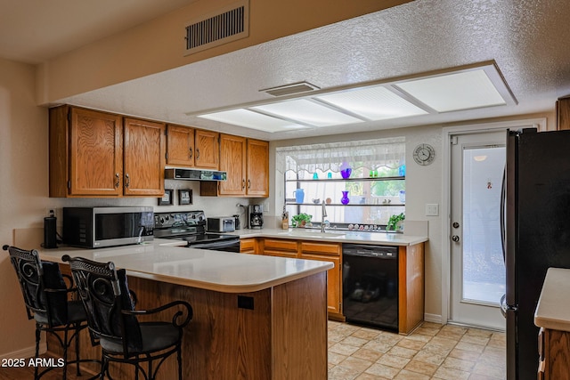 kitchen with sink, a breakfast bar, black appliances, kitchen peninsula, and exhaust hood