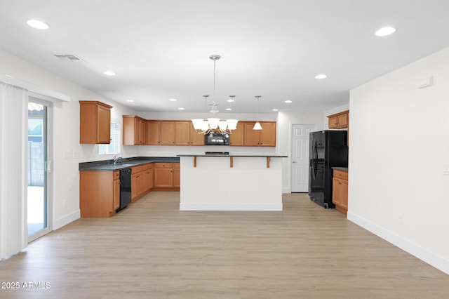 kitchen with light wood-style flooring, a kitchen breakfast bar, visible vents, an inviting chandelier, and black appliances