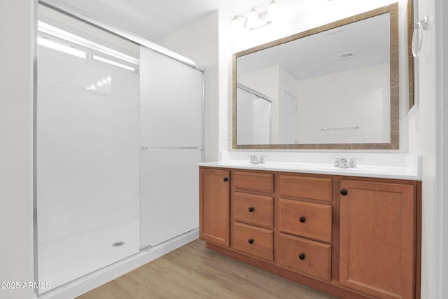 bathroom with double vanity, wood finished floors, a stall shower, and a sink