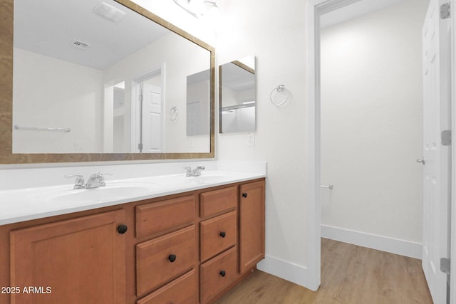 full bath with wood finished floors, a sink, double vanity, baseboards, and visible vents