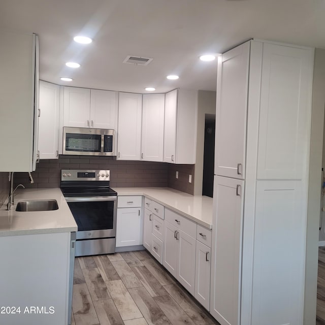 kitchen with sink, light wood-type flooring, white cabinetry, decorative backsplash, and stainless steel appliances