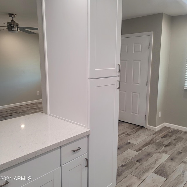 interior space featuring ceiling fan, light stone counters, white cabinets, and light hardwood / wood-style flooring