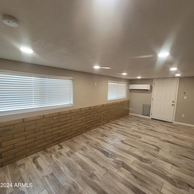 basement with an AC wall unit, brick wall, and light wood-type flooring