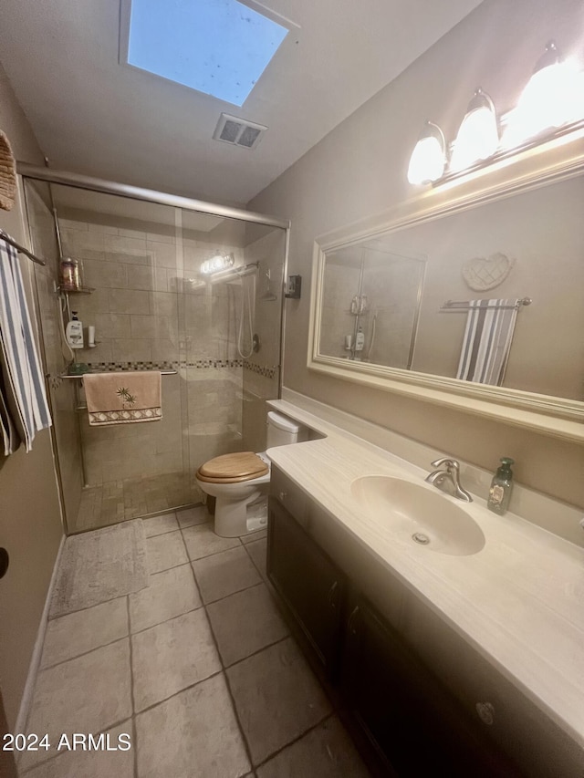 bathroom with a skylight, tile patterned floors, toilet, vanity, and a shower with shower door