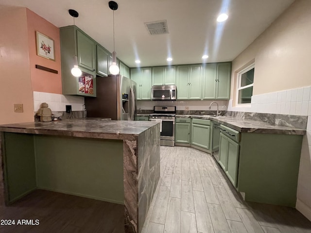 kitchen with hanging light fixtures, green cabinetry, appliances with stainless steel finishes, light hardwood / wood-style floors, and kitchen peninsula