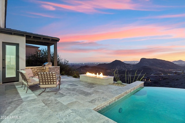 pool at dusk featuring a patio, a mountain view, and an outdoor fire pit