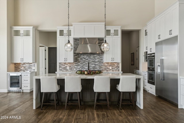 kitchen with built in refrigerator, white cabinetry, wall chimney range hood, and beverage cooler