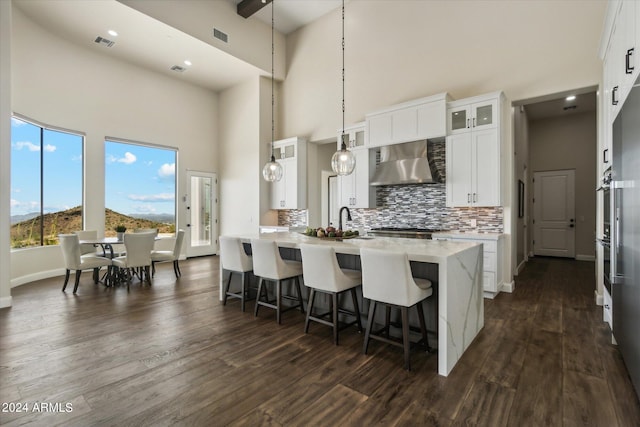 kitchen with pendant lighting, white cabinets, a center island with sink, dark hardwood / wood-style flooring, and wall chimney exhaust hood